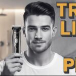 A young man carefully trimming his beard using an electric trimmer in front of a bathroom mirror. The trimmer has LED indicators, and the bathroom setup includes grooming products and bright lighting.