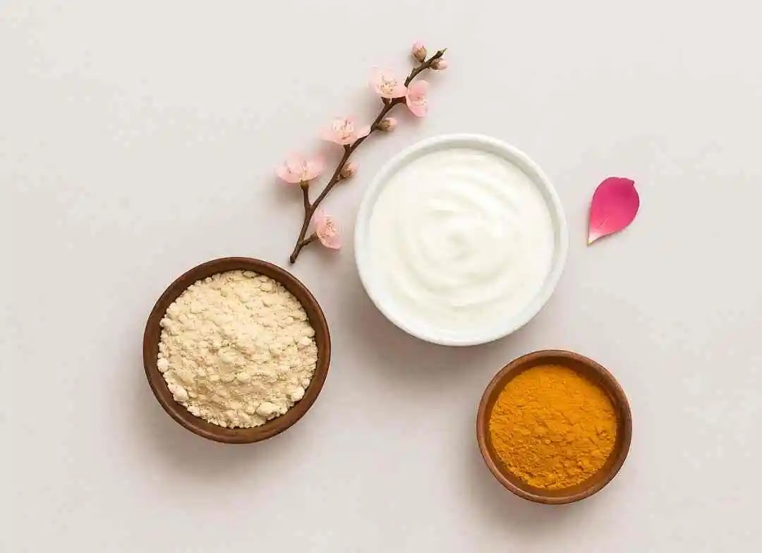 Flat lay of natural ingredients – besan, curd, and turmeric – in bowls for a glowing skin face pack